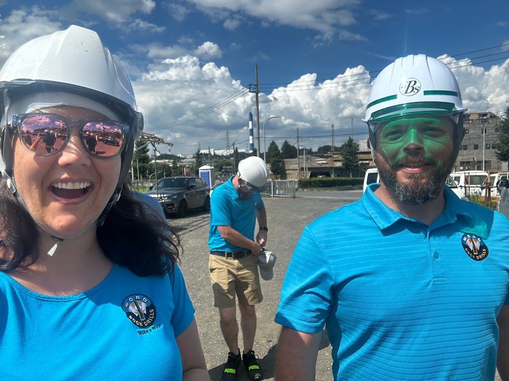 Two Word Rock Drills team members wearing hard hats and blue company shirts at an industrial site.