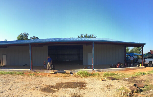 Metal workshop building with a large open garage bay and covered work areas during construction.